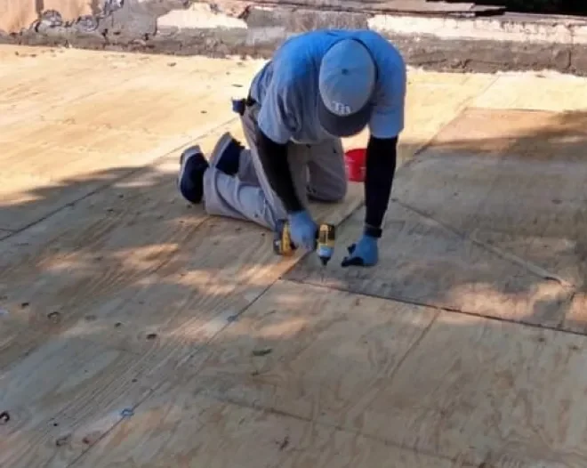 A roofer kneeling to fasten new wooden roof decking